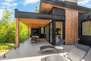 A modern house with a covered patio area featuring outdoor furniture and a view of the surrounding greenery.