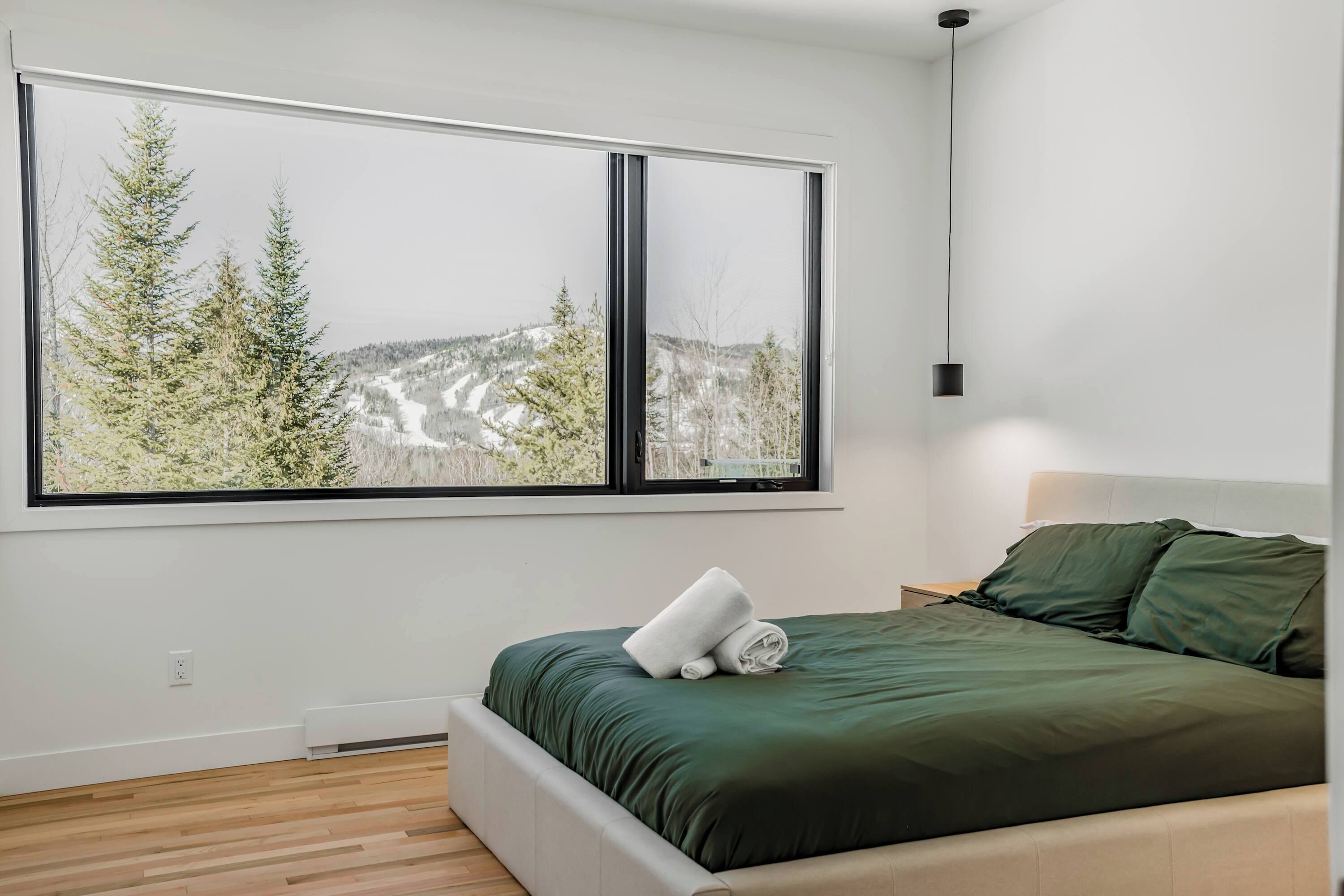 A bedroom with a large window, a bed with green bedding, and a nightstand.
