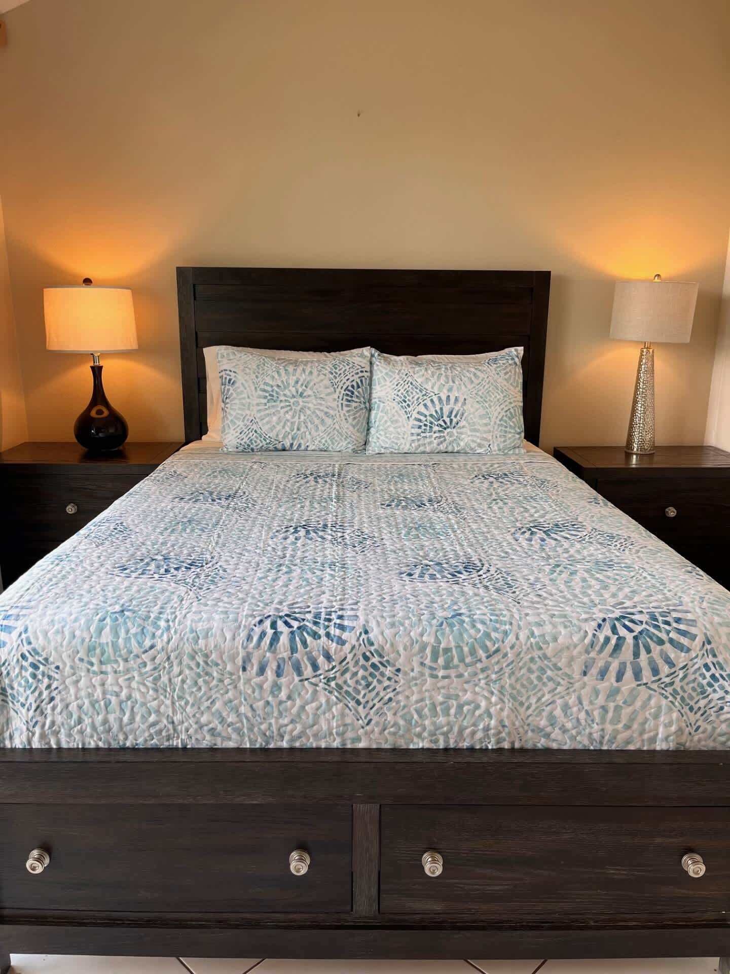 Un lit avec une couvre-lit à motifs, deux oreillers, une tête de lit en bois foncé et deux tables de chevet avec des lampes.