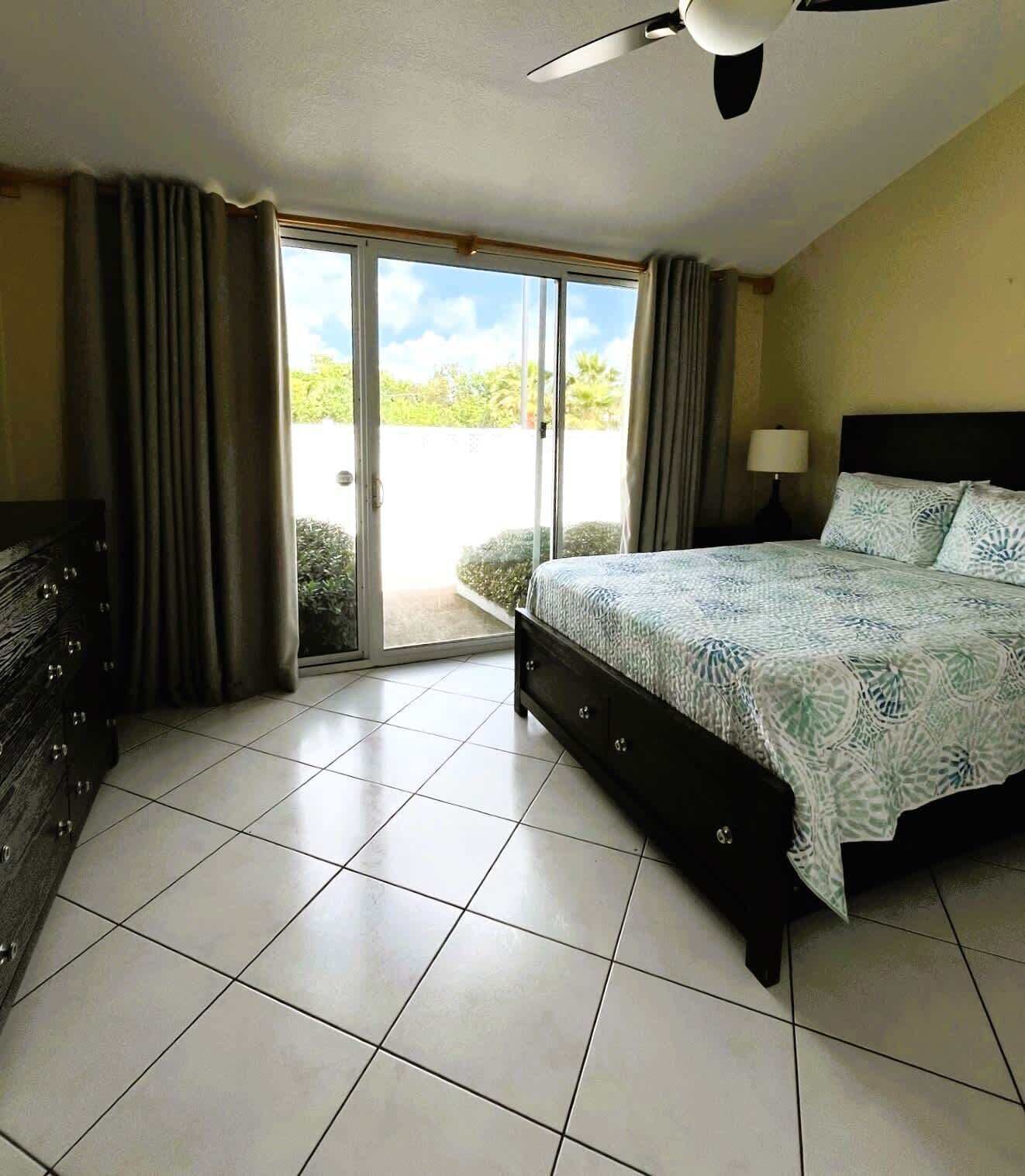 Une chambre à coucher comprenant un lit, une commode, un ventilateur de plafond et une porte-fenêtre coulissante donnant sur un balcon.