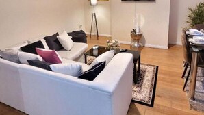 Una sala de estar moderna con un sofá blanco, una mesa de centro, una lámpara de pie y un televisor montado en la pared.