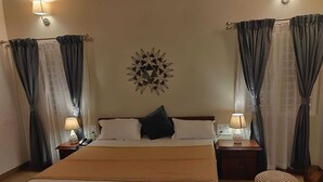Una habitación de hotel con una cama grande, dos mesitas de noche con lámparas, un reloj de pared, un adorno en forma de estrella y un reposapiés redondo.