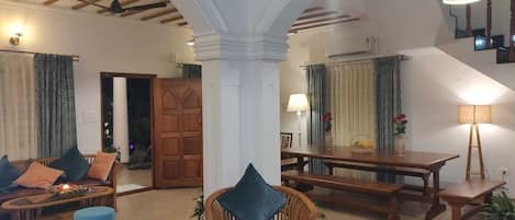 A spacious living area with a high ceiling, wooden beams, and a dining table set with chairs.