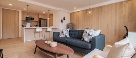A modern living room with a sofa, coffee table, and a kitchen in the background.