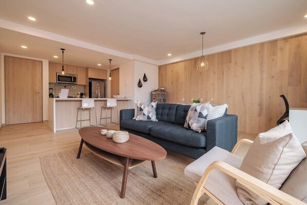 A modern living room with a sofa, coffee table, and a kitchen in the background.