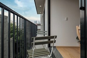 A balcony with a metal railing, a wooden bench, and a view of buildings in the distance.