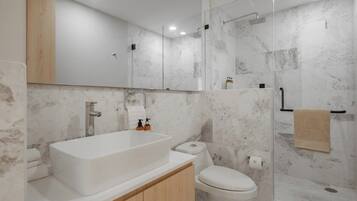 A modern bathroom with a large bathtub, a toilet, and a glass-enclosed shower area.
