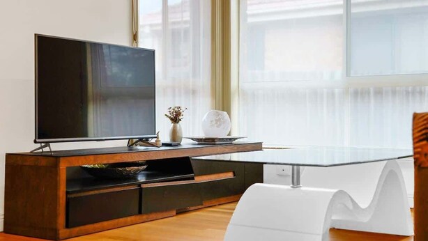 Ein modernes Wohnzimmer mit einem Flachbildfernseher auf einem Holz-TV-Möbel, einem Glastisch und einem weißen Sessel.
