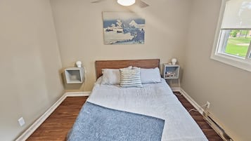 A bedroom with a bed, a ceiling fan, a nightstand, a lamp, and a window with a view of the outdoors.