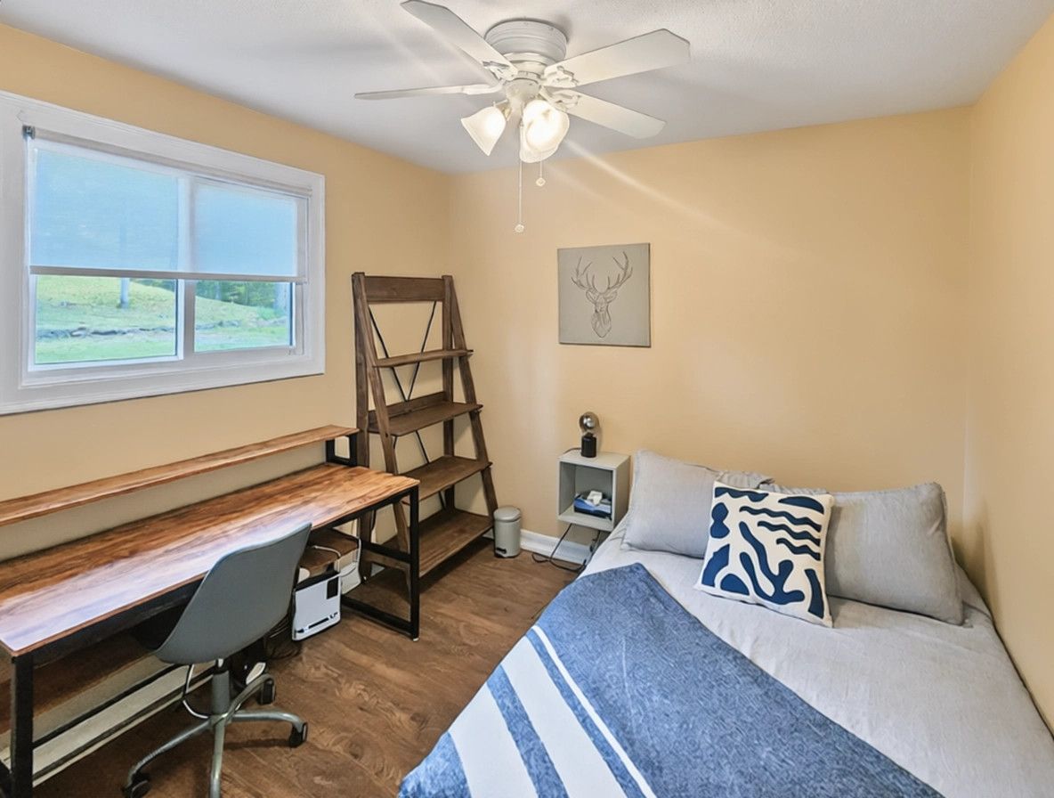 A bedroom with a bed, desk, chair, and a ceiling fan.
