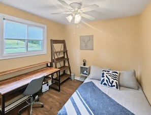 Een slaapkamer met een bed, bureau, stoel en een plafondventilator.