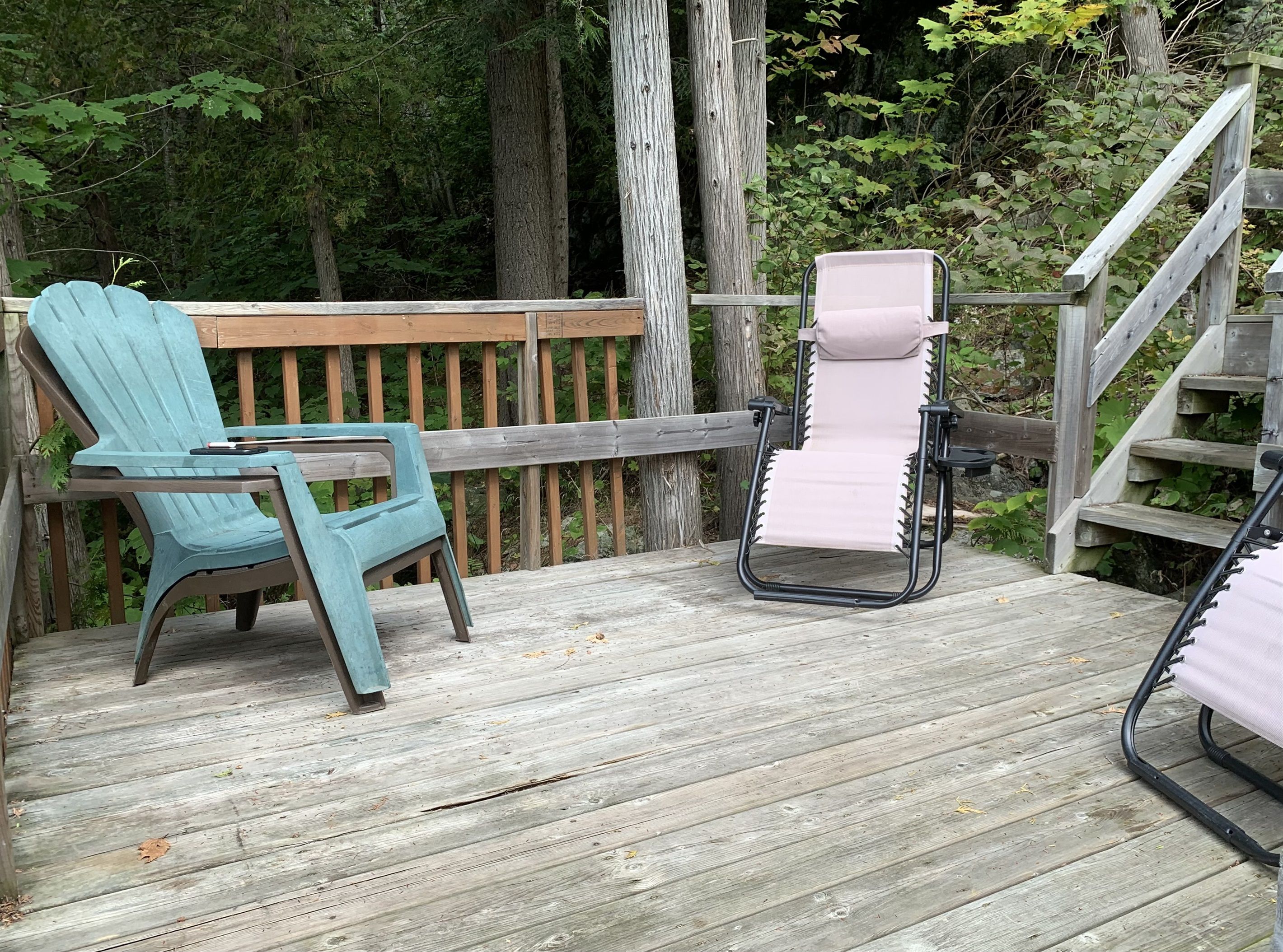Une terrasse en bois avec une chaise Adirondack turquoise et une chaise longue noire dotée d’un coussin rose.