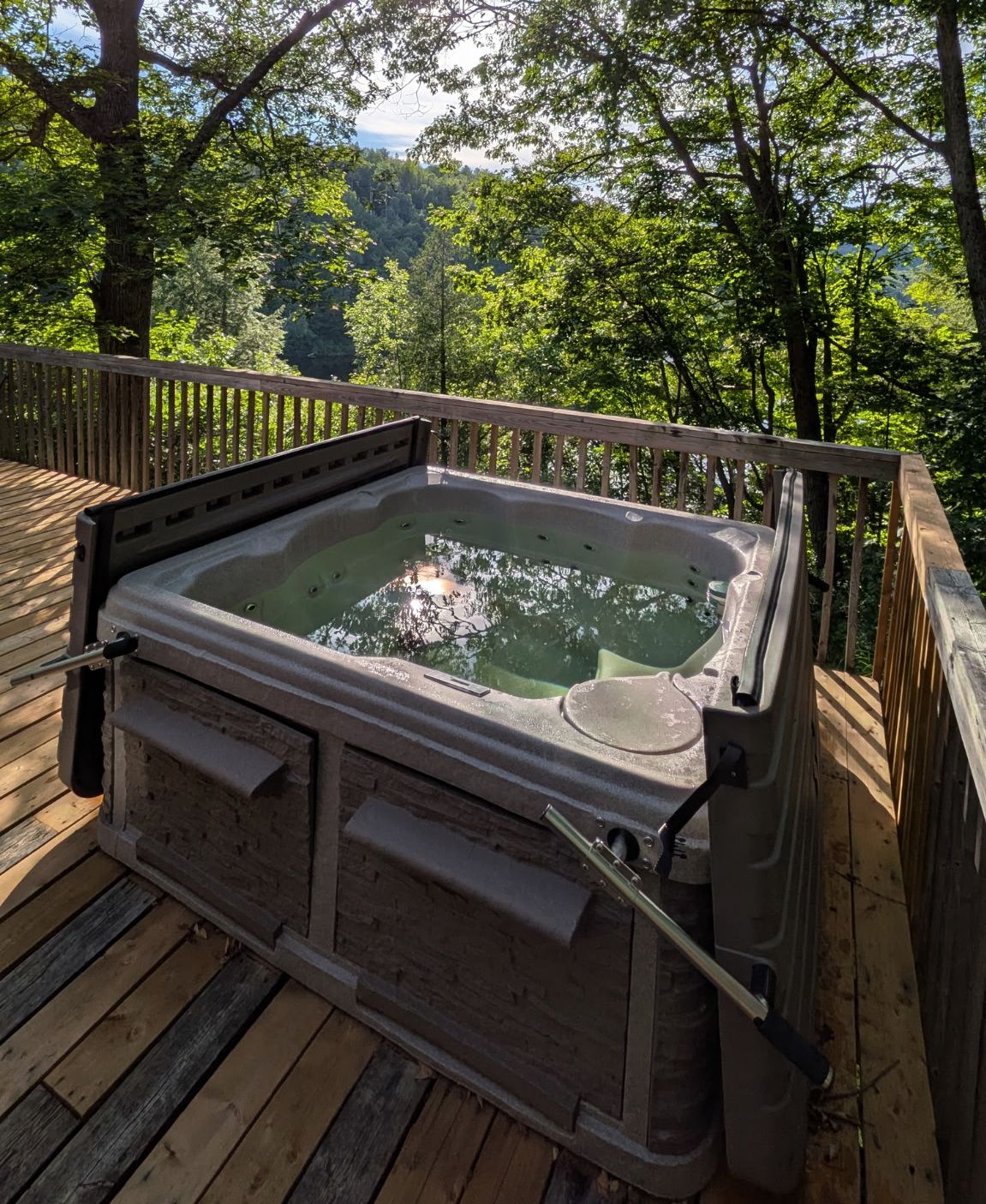 A hot tub on a wooden deck surrounded by trees.