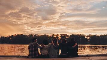 A group of people sitting on a wooden dock by a lake during sunset.