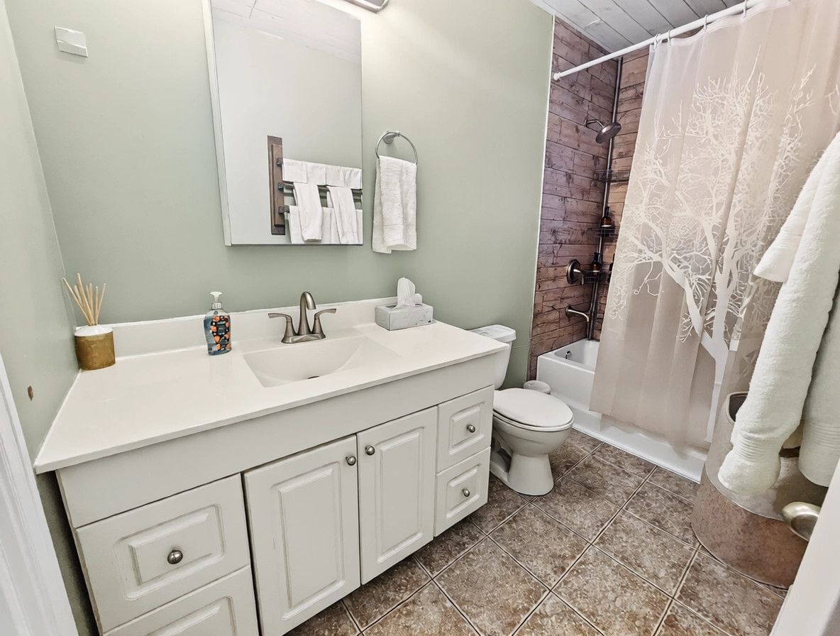 A bathroom with a white sink, mirror, and toilet, a shower with a curtain, and a tiled floor.