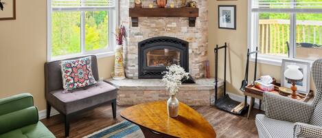 A living room with a stone fireplace, a sofa, a coffee table, and a houndstooth armchair.