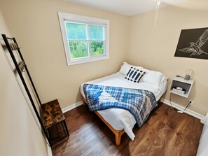 A bedroom with a bed, a window, a bedside table, and a wall-mounted shelf.
