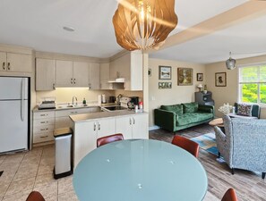 A modern kitchen with a dining area, a green sofa, and a patterned armchair. - Relax on the Shores of Charming Lac McArthur (Val des Monts)