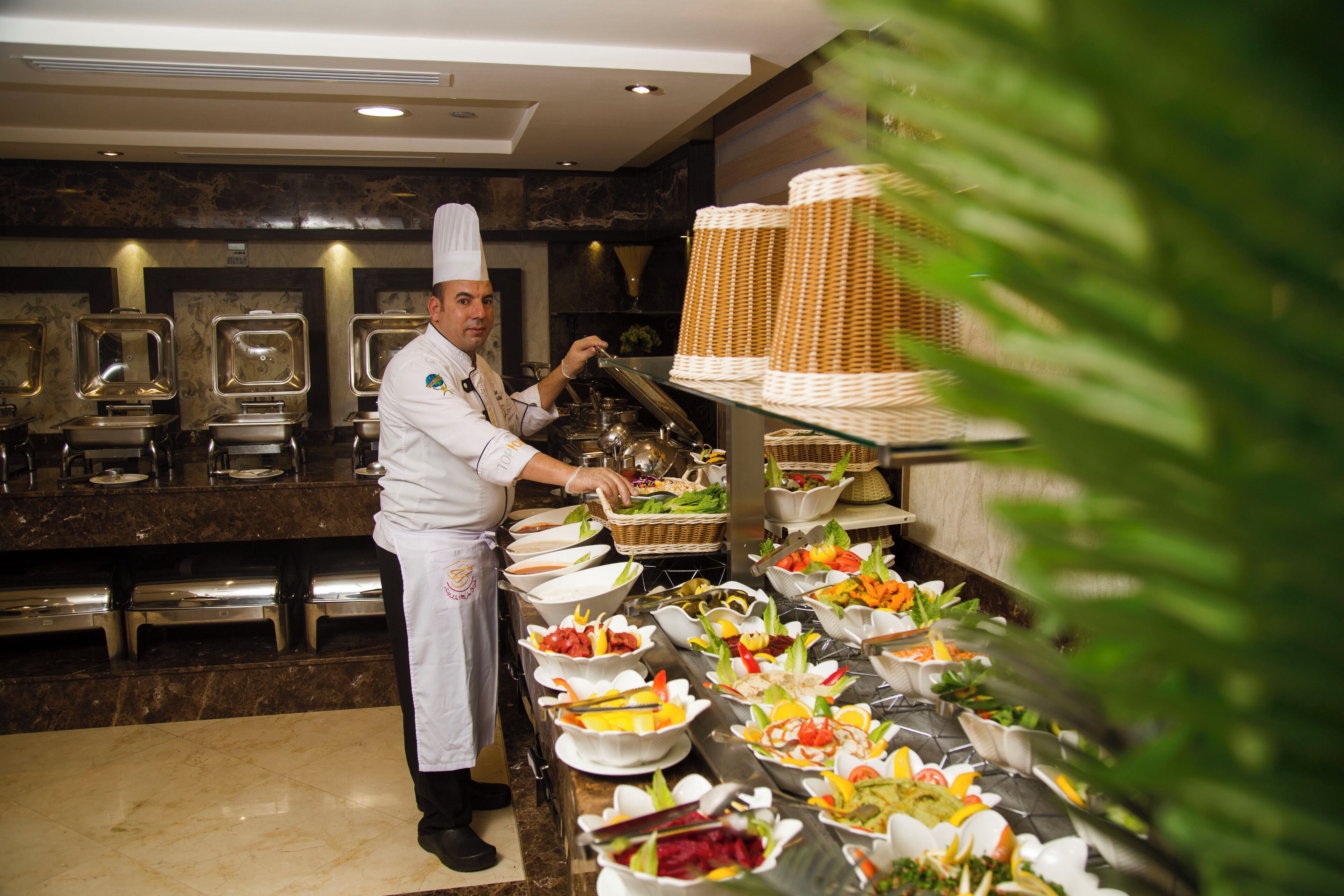 A buffet setup with various food items and a chef preparing food.