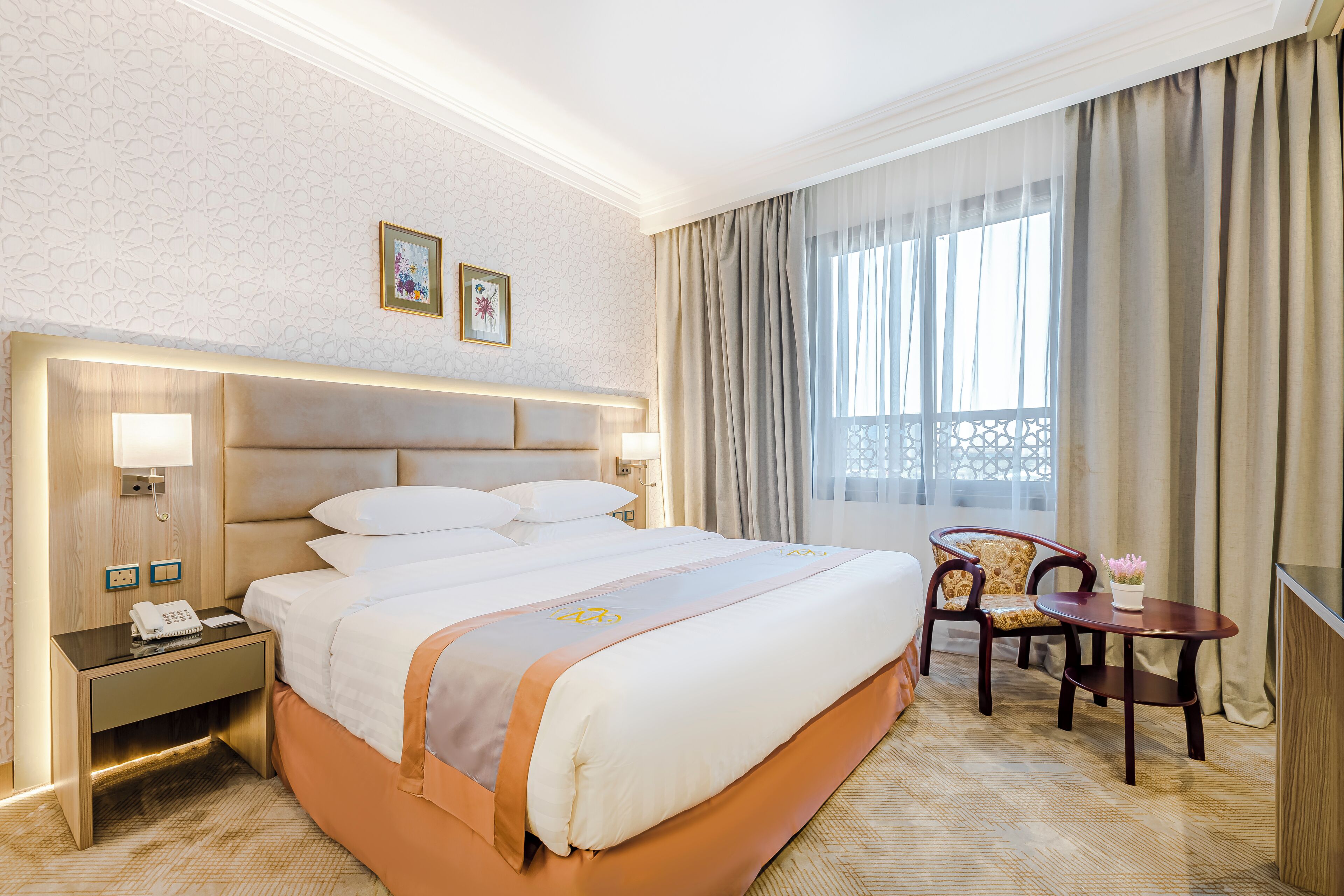 Una habitación de hotel con una cama grande, mesitas de noche, un escritorio, una silla y una ventana con cortinas.