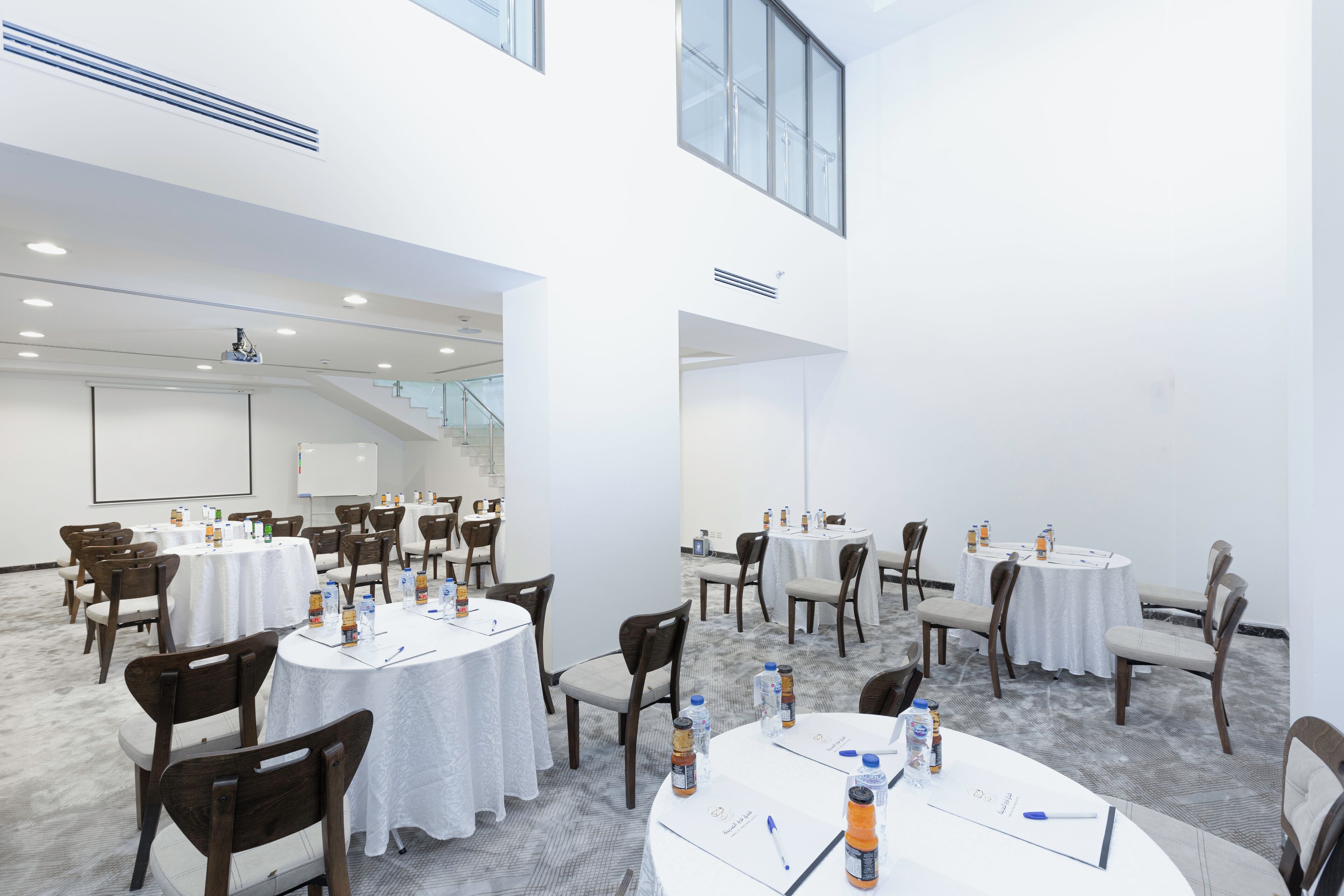 A conference room with multiple tables, chairs, and presentation screens.