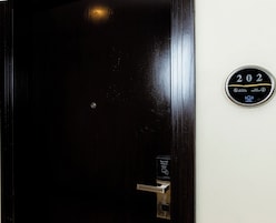 Una puerta de madera oscura con un candado digital y un cartel que indica el número de habitación 202.