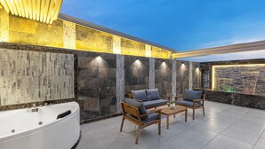 A modern outdoor seating area with a large bathtub, wooden furniture, and a stone wall with illuminated panels. - Faraj Al Madina Hotel (Madinah)