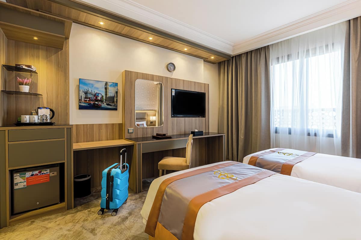 Habitación de hotel con dos camas, un escritorio, un televisor, un reloj y una ventana con cortinas.