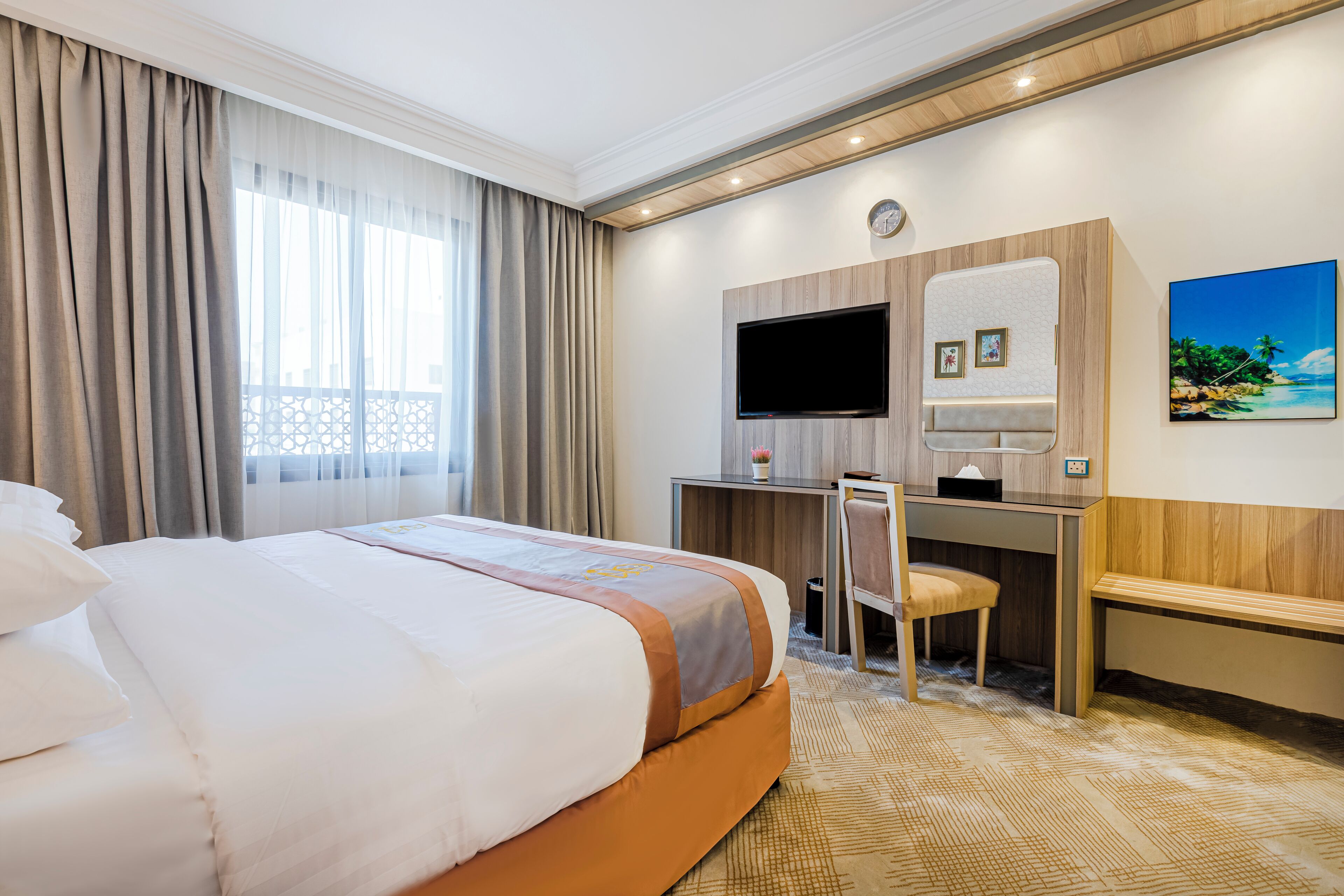 A hotel room with a large bed, a desk with a chair, a television, and a painting on the wall.