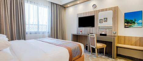 A hotel room with a large bed, a desk with a chair, a television, and a painting on the wall.