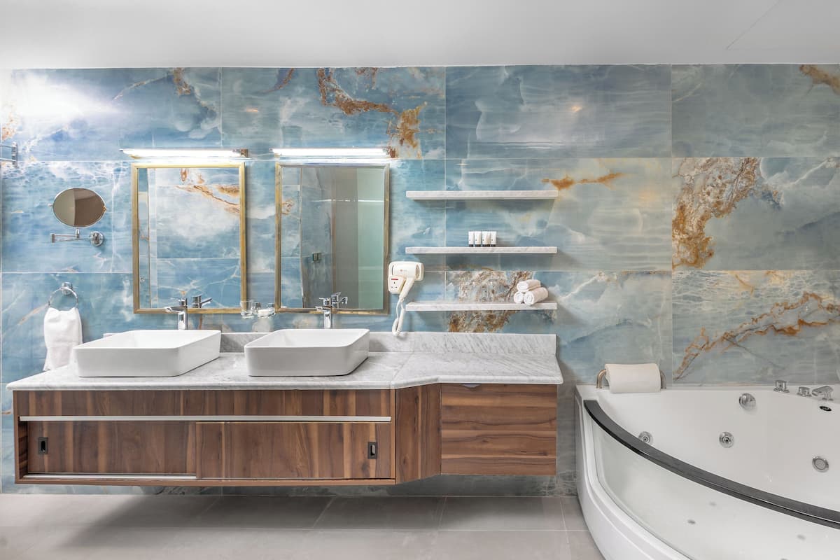 Un baño moderno con dos lavamanos, un espejo grande, un mueble de tocador con armarios de madera, una bañera y paredes con diseño de mármol.