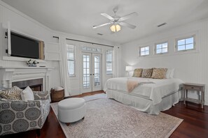 A spacious bedroom with a large bed, a television mounted on the wall, a fireplace, and a ceiling fan.