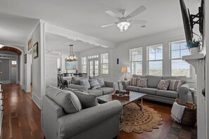 A spacious living room with a grey sofa set, a coffee table, and a dining area with a chandelier.