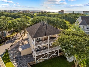 A two-story house with a balcony, surrounded by trees and a view of the sea.
