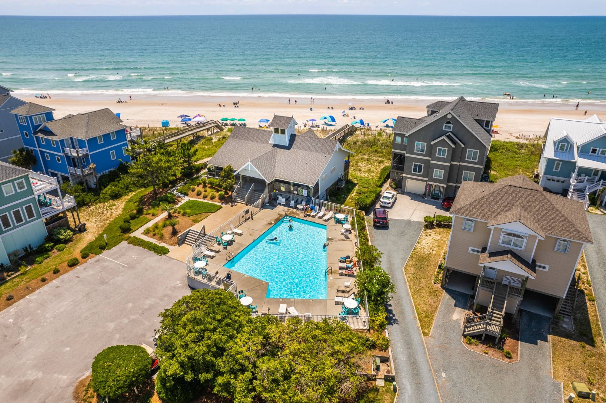 A residential area with a swimming pool surrounded by houses, a beach, and ocean views.