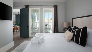 A hotel room with a bed, a TV, a desk, a chair, a lamp, and a view of the outside.