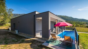 A modern building with a pool, outdoor seating, and a view of the hills. - Villa Rhapsody by Villas Guide (Buzet)