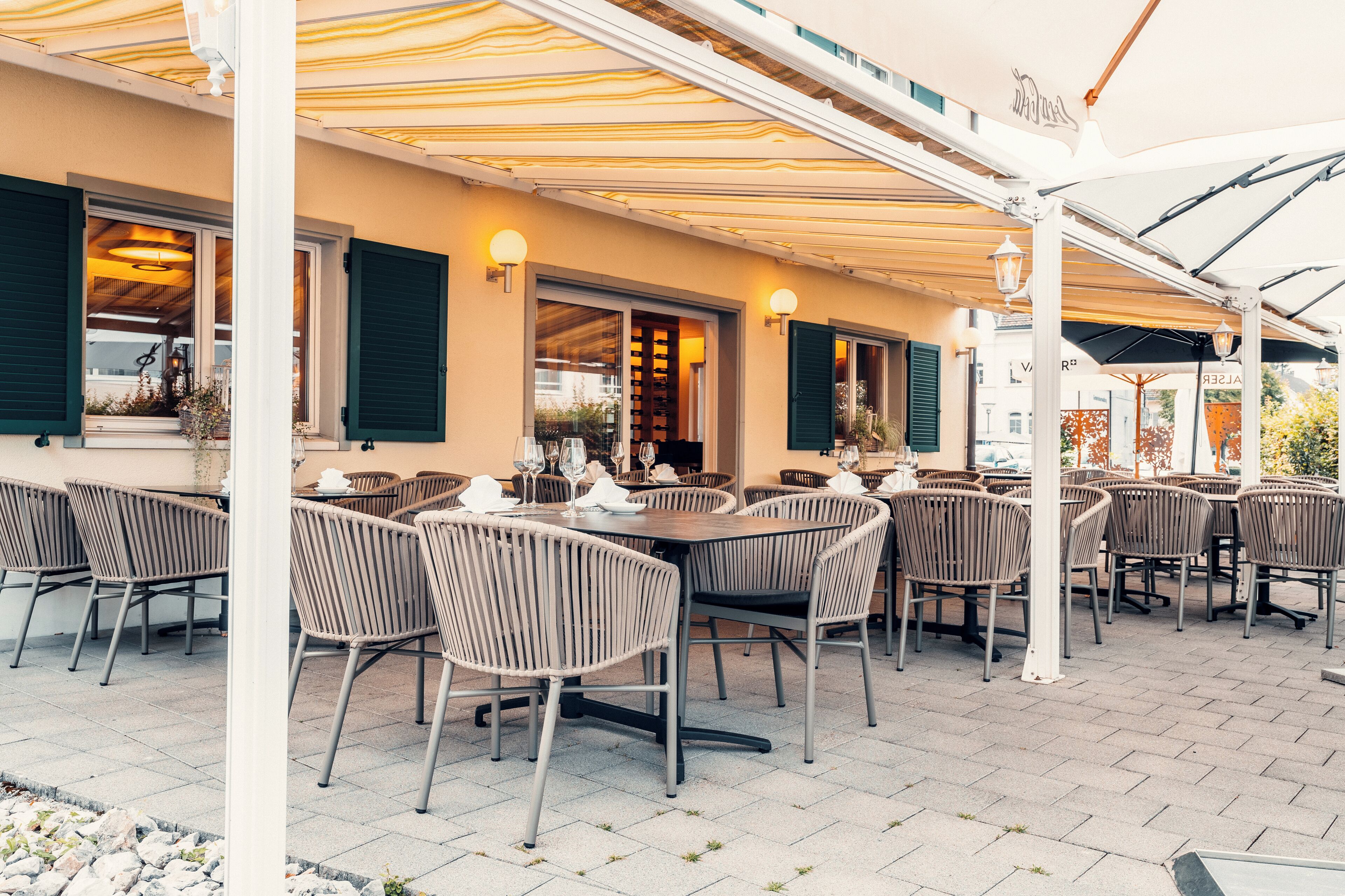 Een terras buiten met meerdere tafels en stoelen, een overdekte zithoek en uitzicht op de straat.