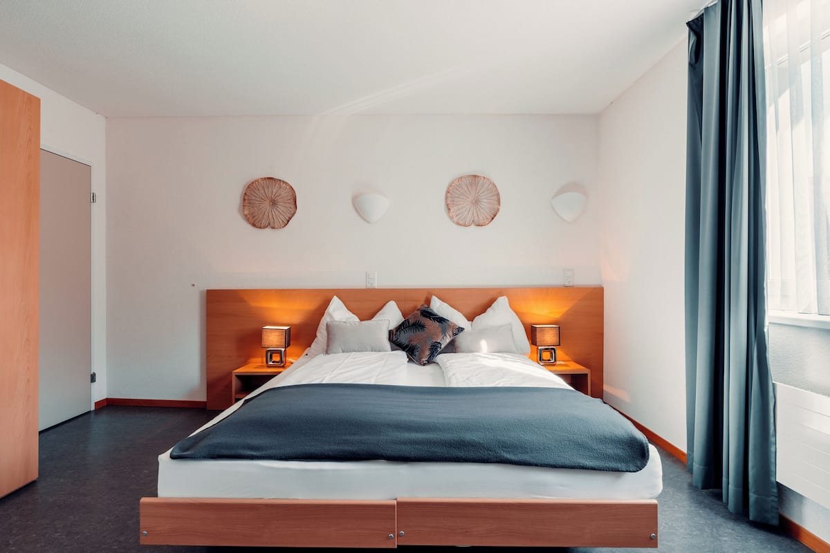Un lit bien fait, avec une tête de lit en bois, deux tables de chevet avec des lampes et des œuvres d’art décoratives accrochées au mur.