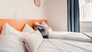 Een keurig opgemaakt bed met witte lakens en een houten hoofdbord, een wandlamp en een raam met gordijnen.