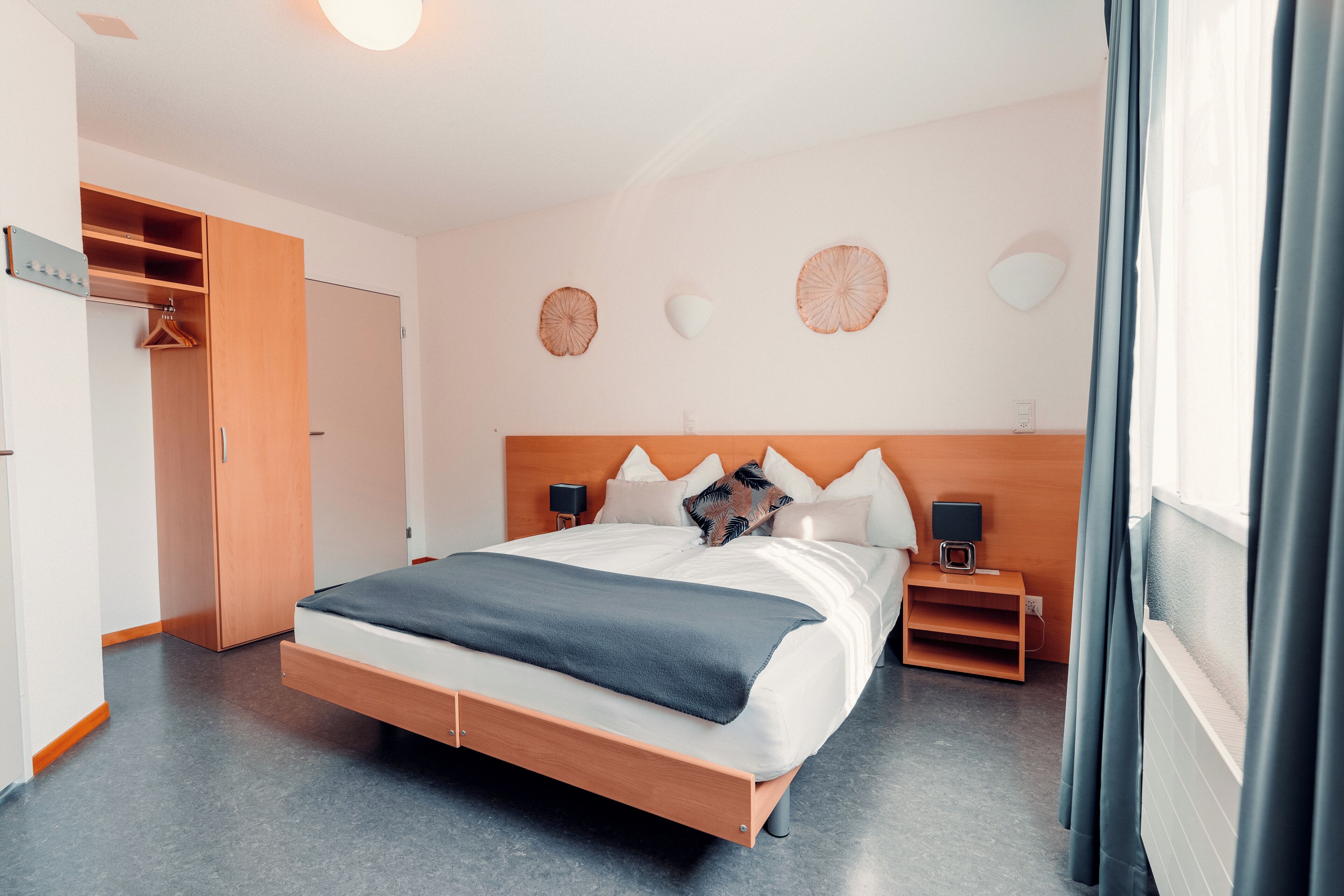 A modern hotel room with a wooden bed, bedside tables, a wardrobe, and decorative wall art.