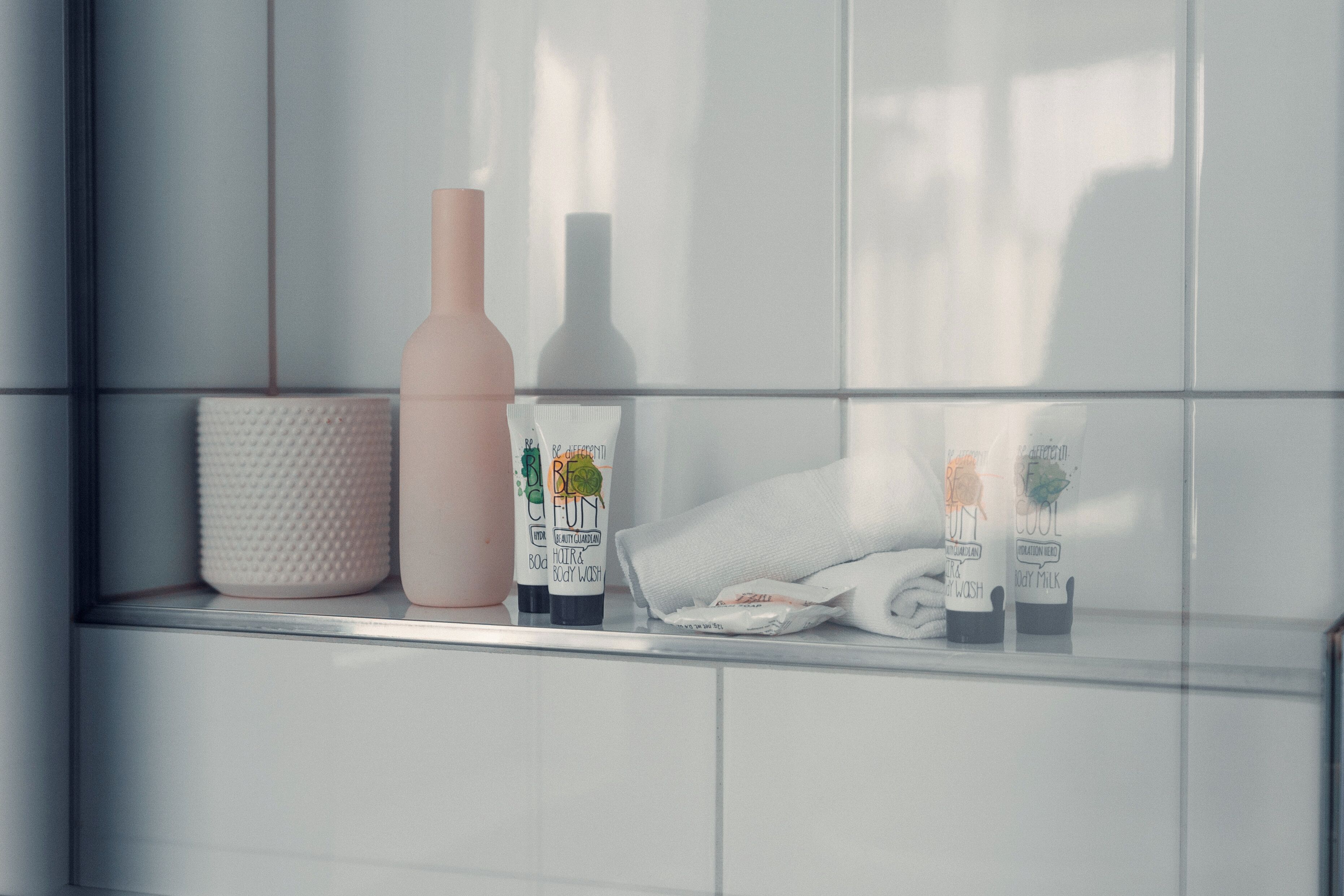 A bathroom shelf with a white textured container, a pink bottle, and two bottles labeled "Body Milk" and "Body Wash".