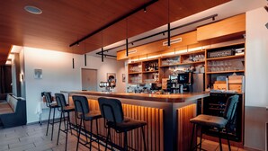 Een moderne bar met een houten toog, meerdere barkrukken en planken vol glazen en flessen.