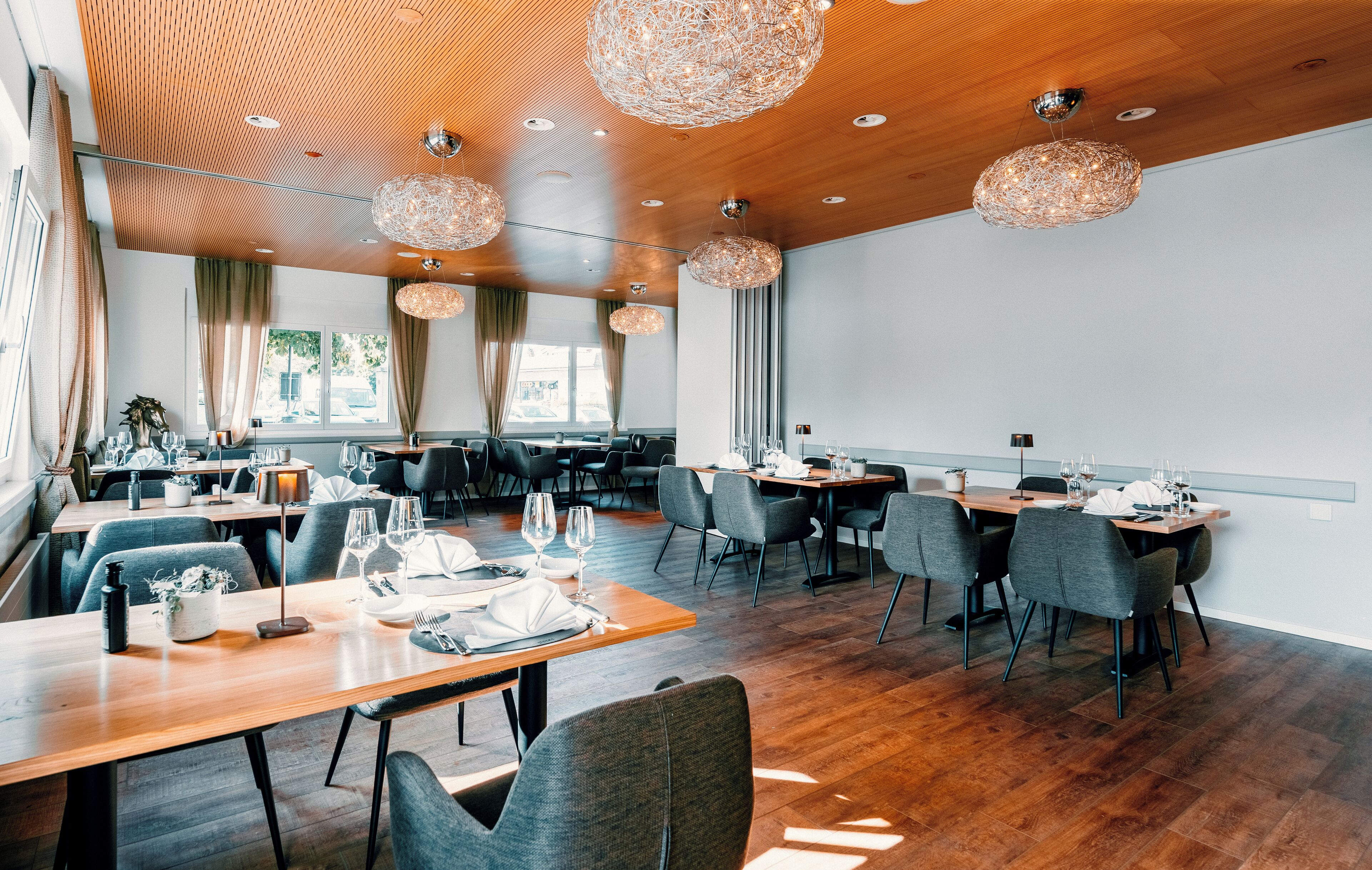 A modern restaurant with wooden flooring and ceiling, large chandeliers, and a mix of table settings.