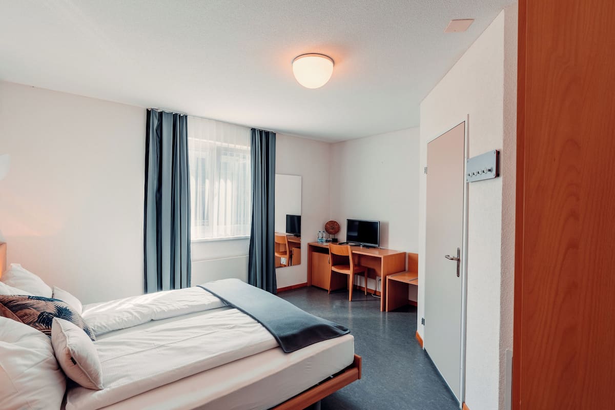 Une chambre d’hôtel avec un lit, un bureau, une chaise, une télévision et une porte.