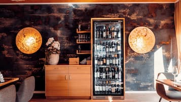 Zona de bar moderna con refrigerador para vino, armarios de madera y dos grandes luces fijadas a la pared.