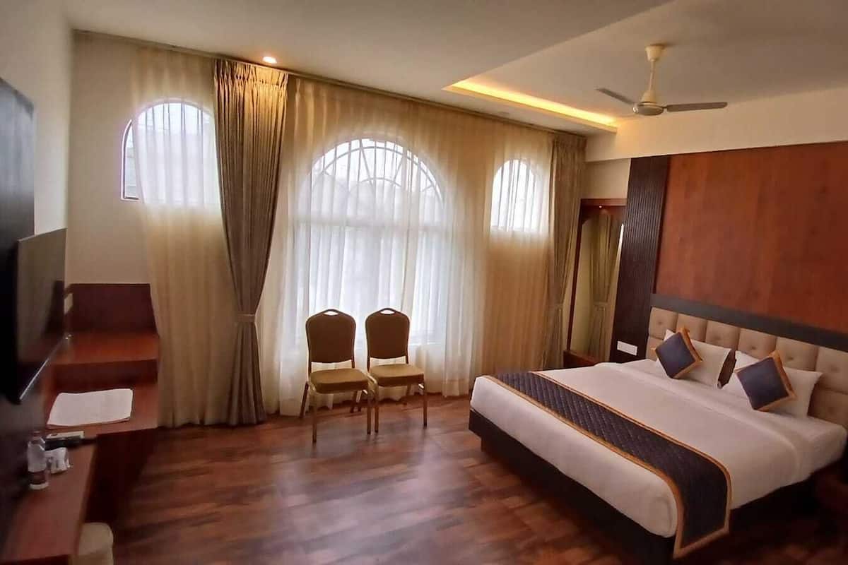 A hotel room with a large bed, two chairs, a desk, and a TV.