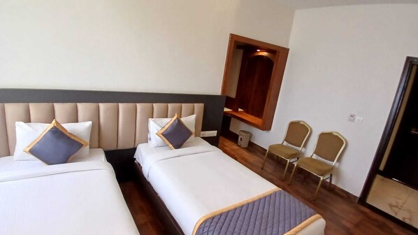Habitación de hotel con dos camas, cabecera de madera, un pequeño rincón de descanso con sillas y un espejo en la pared.