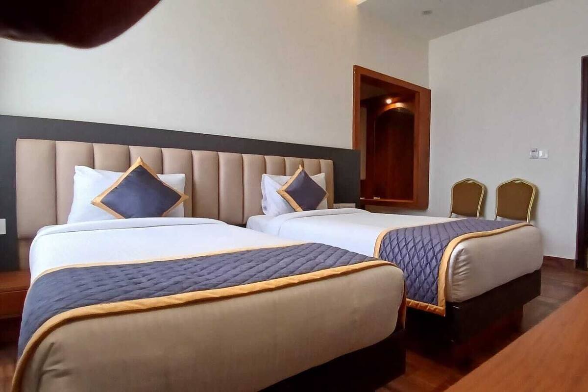 A hotel room with two beds, each with a headboard and pillows, a wooden table, and a door.