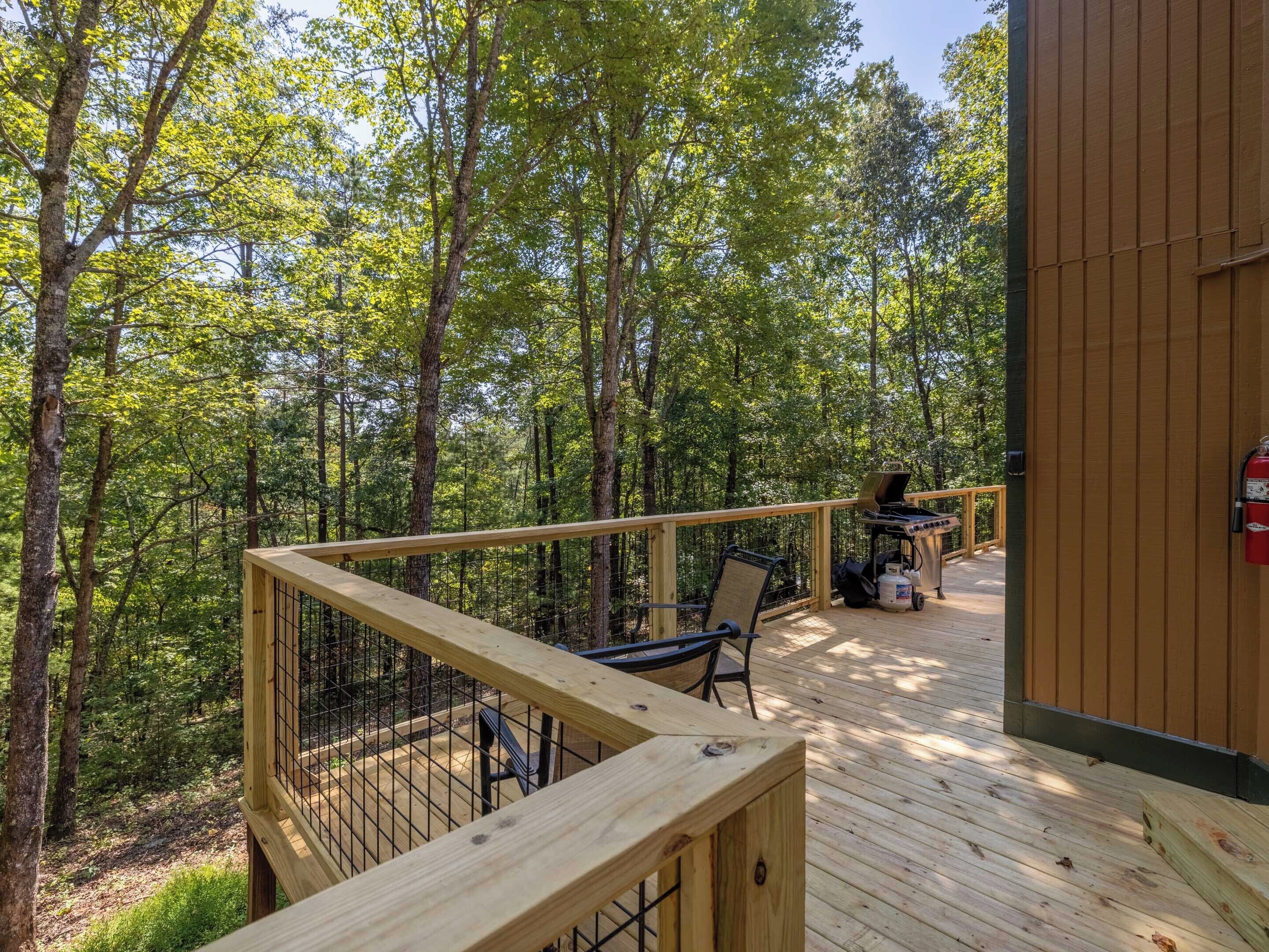 A wooden deck with a metal railing, a grill, and a fire extinguisher.